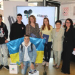 Zdjęcie grupowe, na którym znajdują się trzej nastoletni chłopcy ustawieni wokół dużej flagi Ukrainy. Obok laureatów, stoją cztery uśmiechnięte kobiety. Pierwsza, ubrana we wzorzystą sukienkę, ma jasne i mocno kręcone włosy. Kolejna, rudowłosa, wyróżniająca się jasnożółtą bluzką, trzyma w dłoni teczkę z ekslibrisem biblioteki. Nieco dalej stoi nauczycielka i współorganizatorka konkursu o czarnych włosach, ubrana w kremowy garnitur. Zwieńczeniem grupy jest postać dyrektor biblioteki w czarnym garniturze.