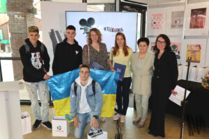 Zdjęcie grupowe, na którym znajdują się trzej nastoletni chłopcy ustawieni wokół dużej flagi Ukrainy. Obok laureatów, stoją cztery uśmiechnięte kobiety. Pierwsza, ubrana we wzorzystą sukienkę, ma jasne i mocno kręcone włosy. Kolejna, rudowłosa, wyróżniająca się jasnożółtą bluzką, trzyma w dłoni teczkę z ekslibrisem biblioteki. Nieco dalej stoi nauczycielka i współorganizatorka konkursu o czarnych włosach, ubrana w kremowy garnitur. Zwieńczeniem grupy jest postać dyrektor biblioteki w czarnym garniturze.