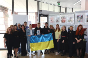 Zdjęcie grupowe, w centrum którego znajduje się wyróżniony zespół z Ukrainy. Trzech nastolatków trzyma przed sobą rozłożoną flagę Ukrainy, a z obu stron otaczają ich pracownicy biblioteki, w znakomitej większości ubrani na czarno.