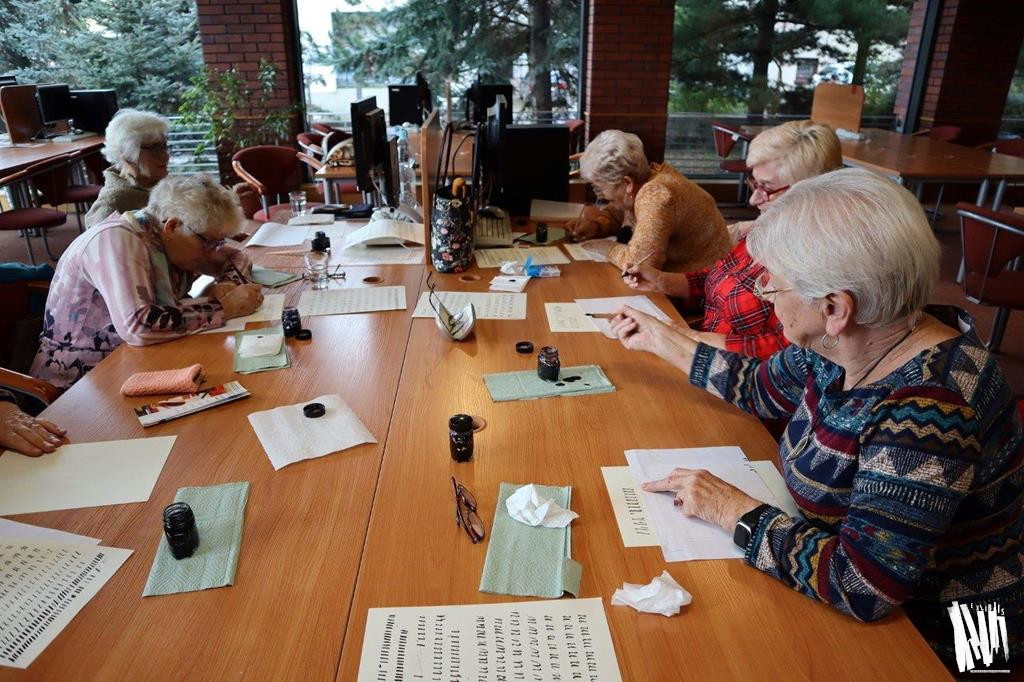 Przy stole w Czytelni Naukowej siedzi sześć siwowłosych kobiet. Każda z uczestniczek warsztatów pochyla się nad kartką papieru, którą zapełnia wykaligrafowanymi znakami, tworzonymi przy pomocy specjalnych piór i atramentów.