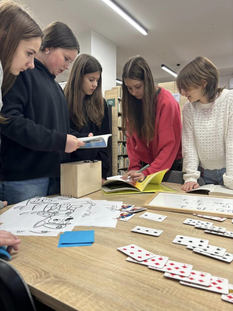 Pięć dziewcząt rozwiązuje zagadki, które rozłożono na stoliku w Filii Bory. Wśród zagadek widać karty do gry, kolorowanki z psiego patrolu, działania matematyczne i jakieś książki.